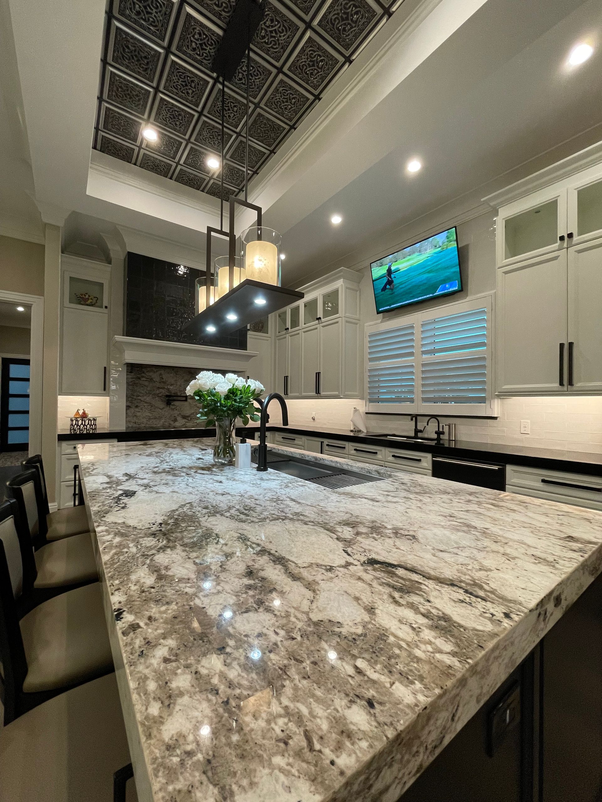 Bright modern kitchen with a large marble island, pendant lights, and a wall-mounted TV above the sink