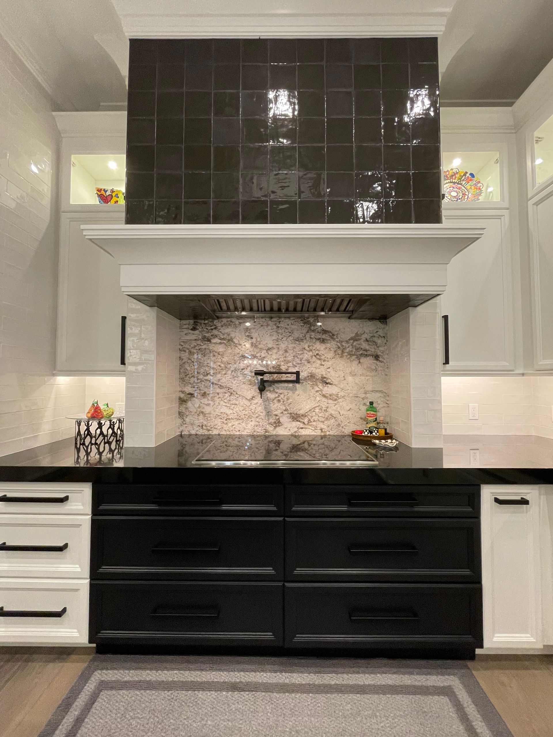 Modern kitchen with black range hood, white cabinets, black lower cabinets, and tiled backsplash