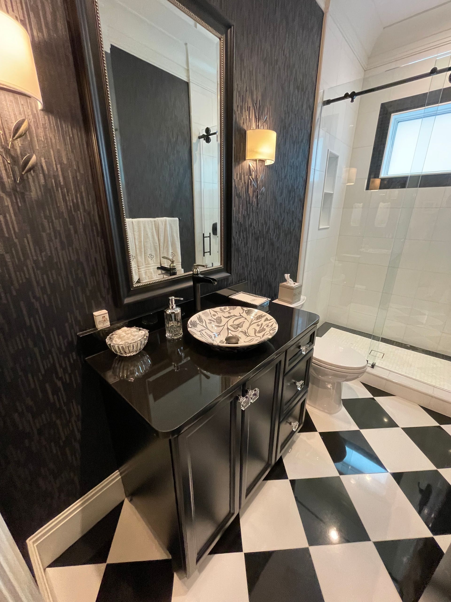 Black-and-white bathroom vanity with mirror, sink, and tiled floor; shower visible in the background