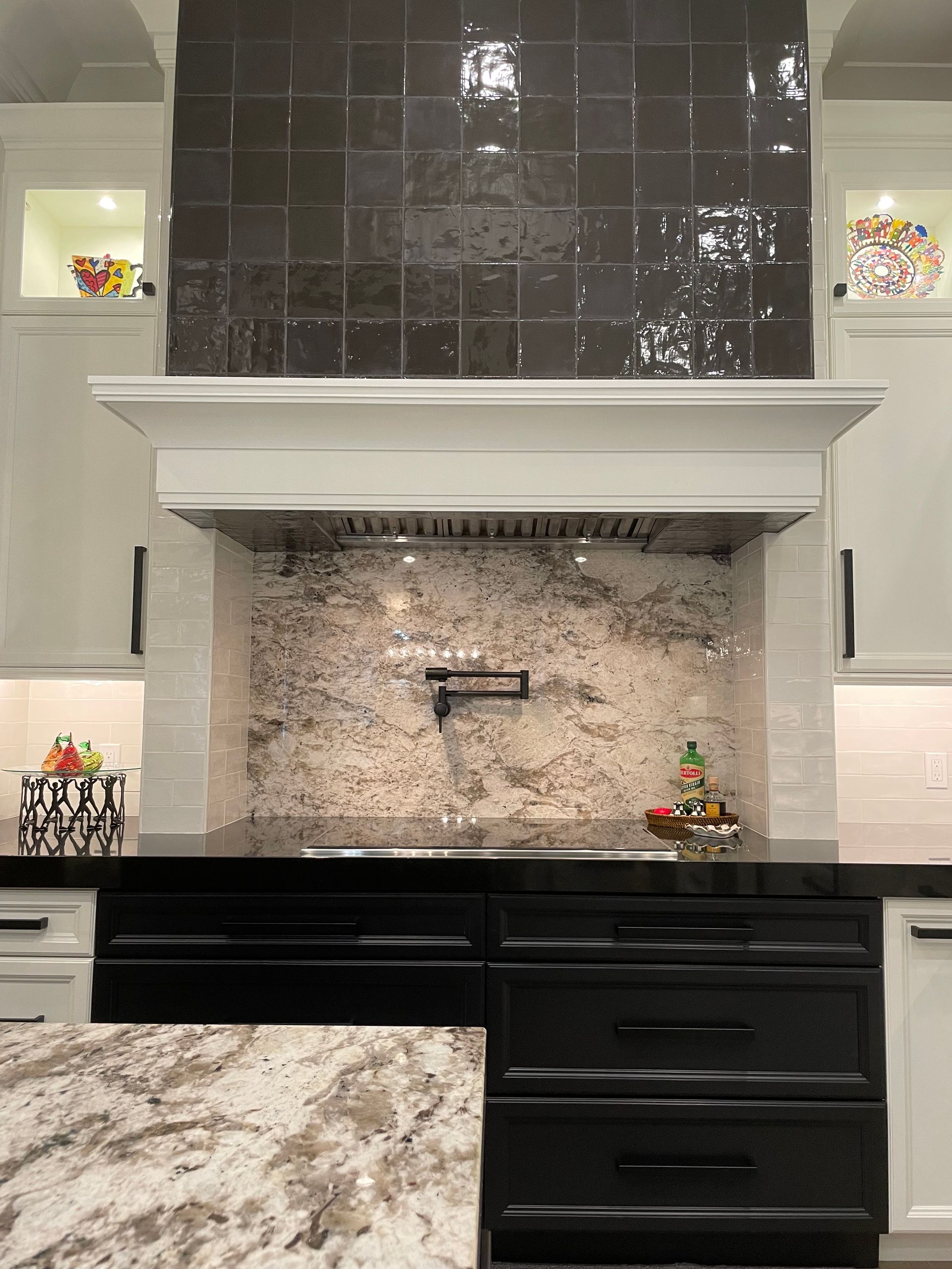 Modern kitchen with black and white cabinetry, marble countertops, and a black tile backsplash above the range.