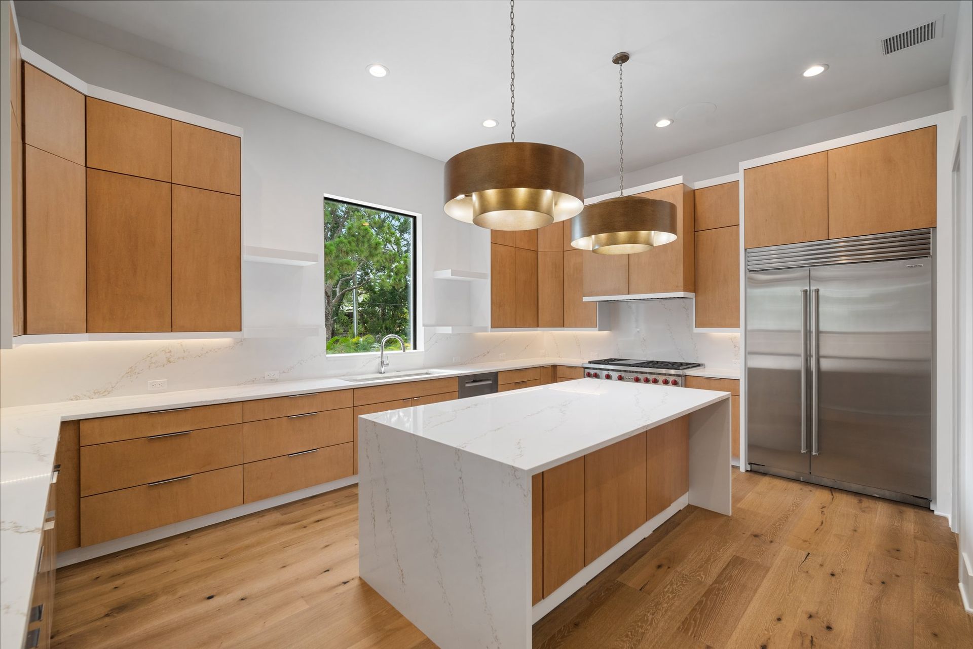 Modern kitchen with wood cabinets, white island, pendant lights, and stainless steel appliances