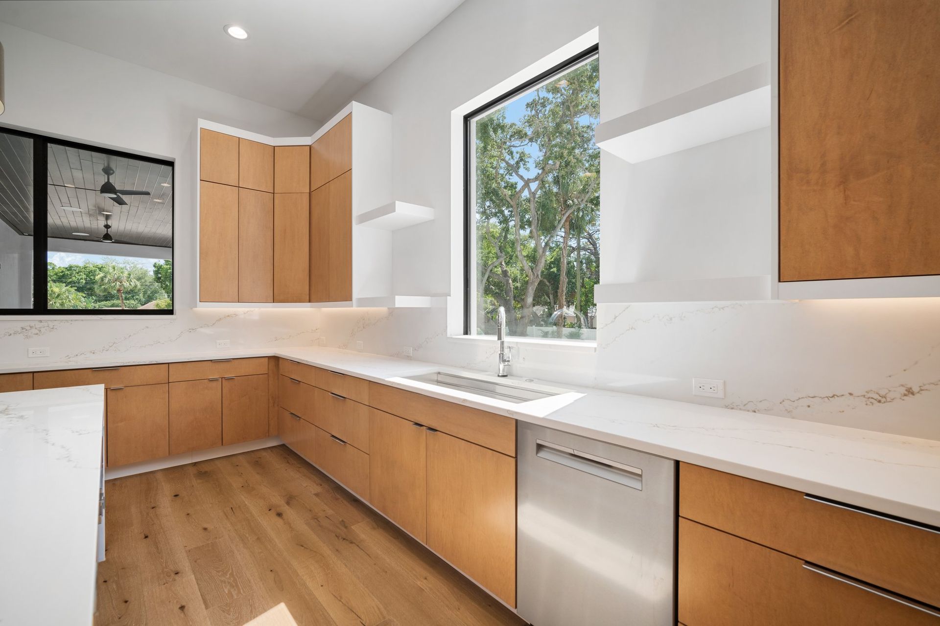 Bright modern kitchen with wood cabinets, white countertops, and large windows overlooking trees