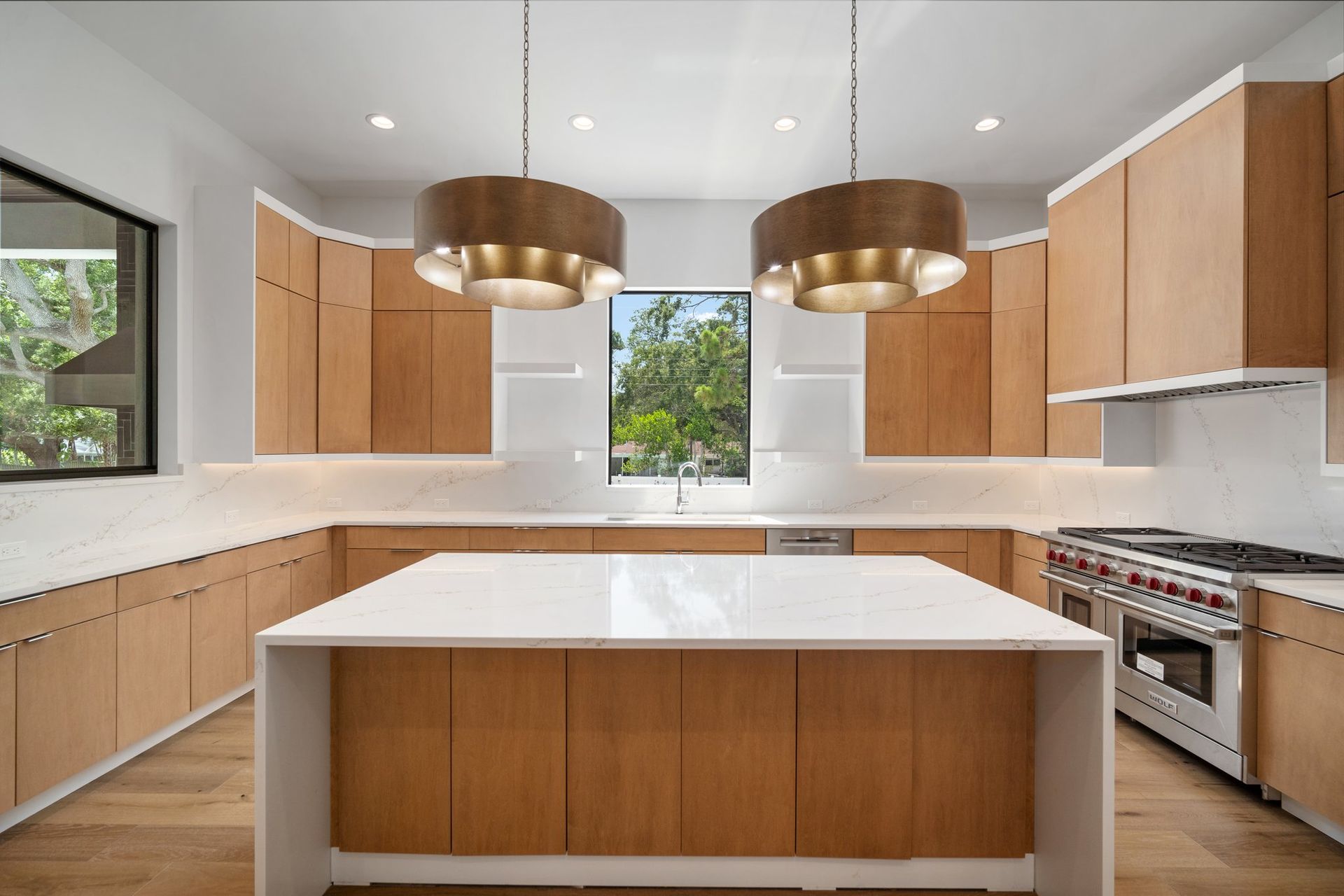 Modern kitchen with wood cabinets, white countertops, stainless stove, and two brass pendant lights.