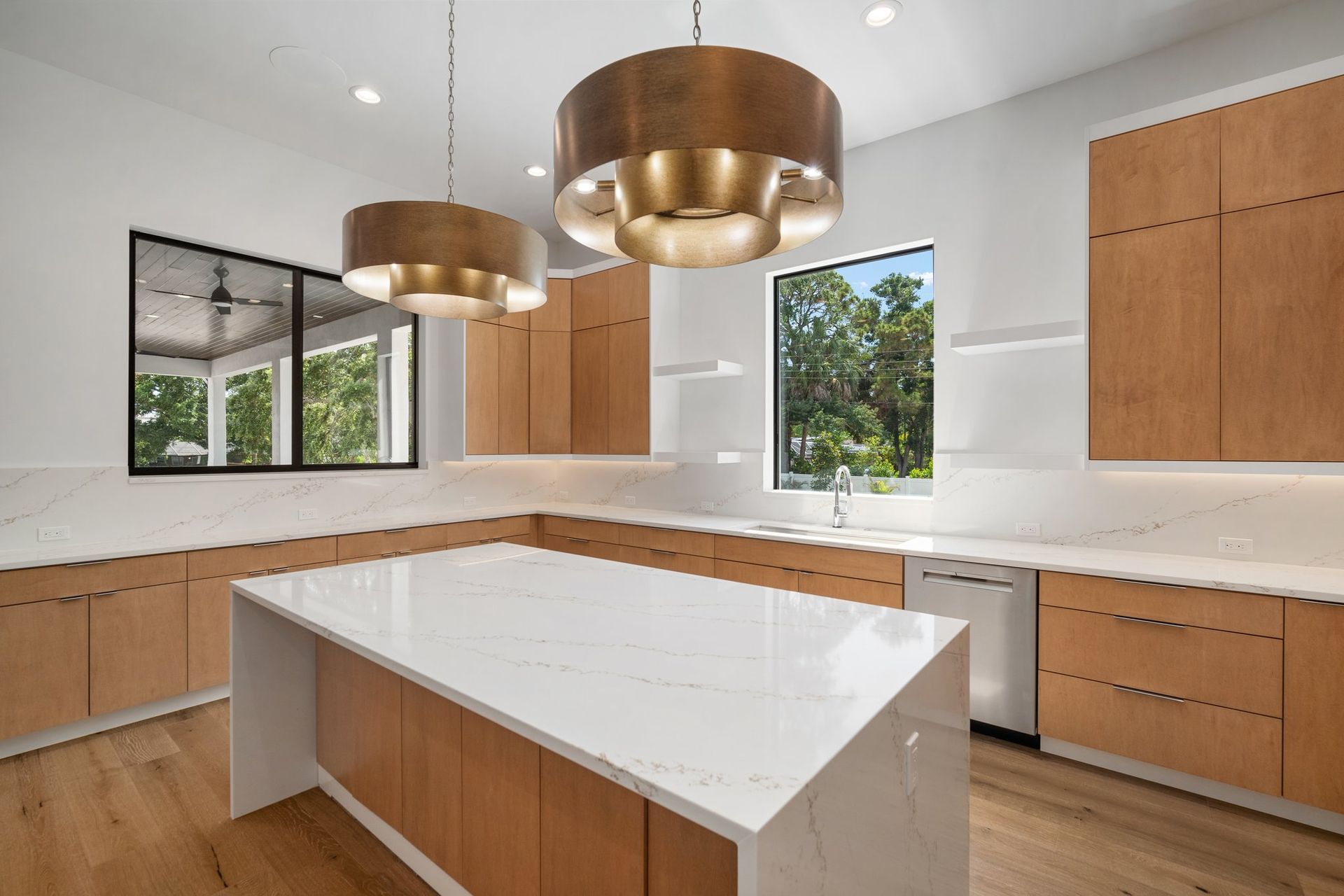 Modern kitchen with white countertops, wood cabinets, large island, and brass pendant lights