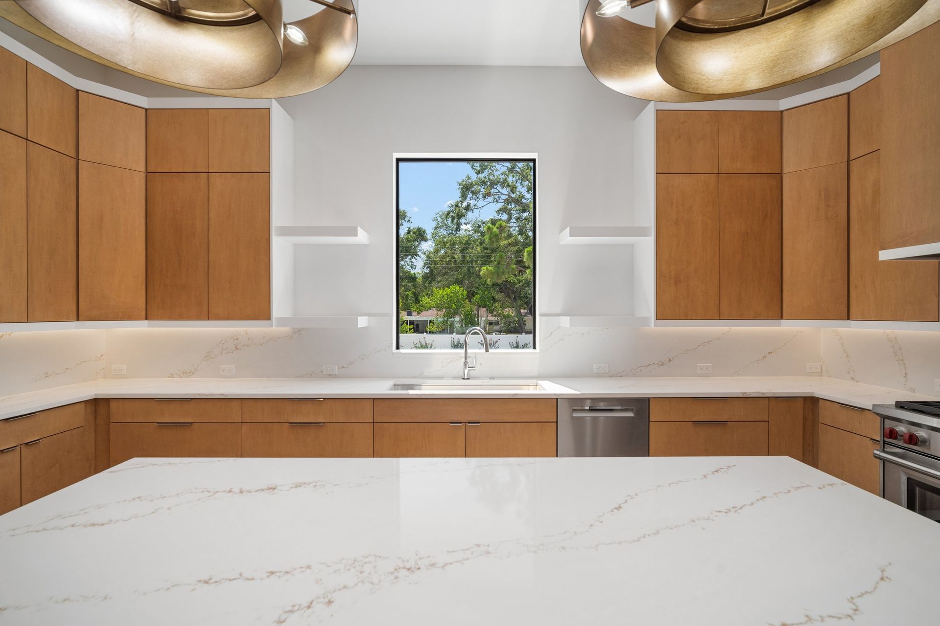 Modern kitchen with wood cabinets, white marble counters, and a window view of trees
