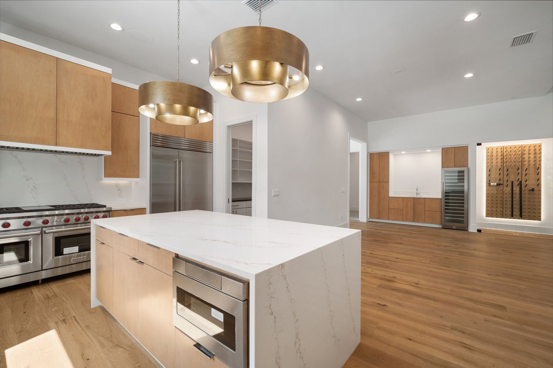 Modern open-plan kitchen with white island, wood cabinets, gold pendant lights, and hardwood floors