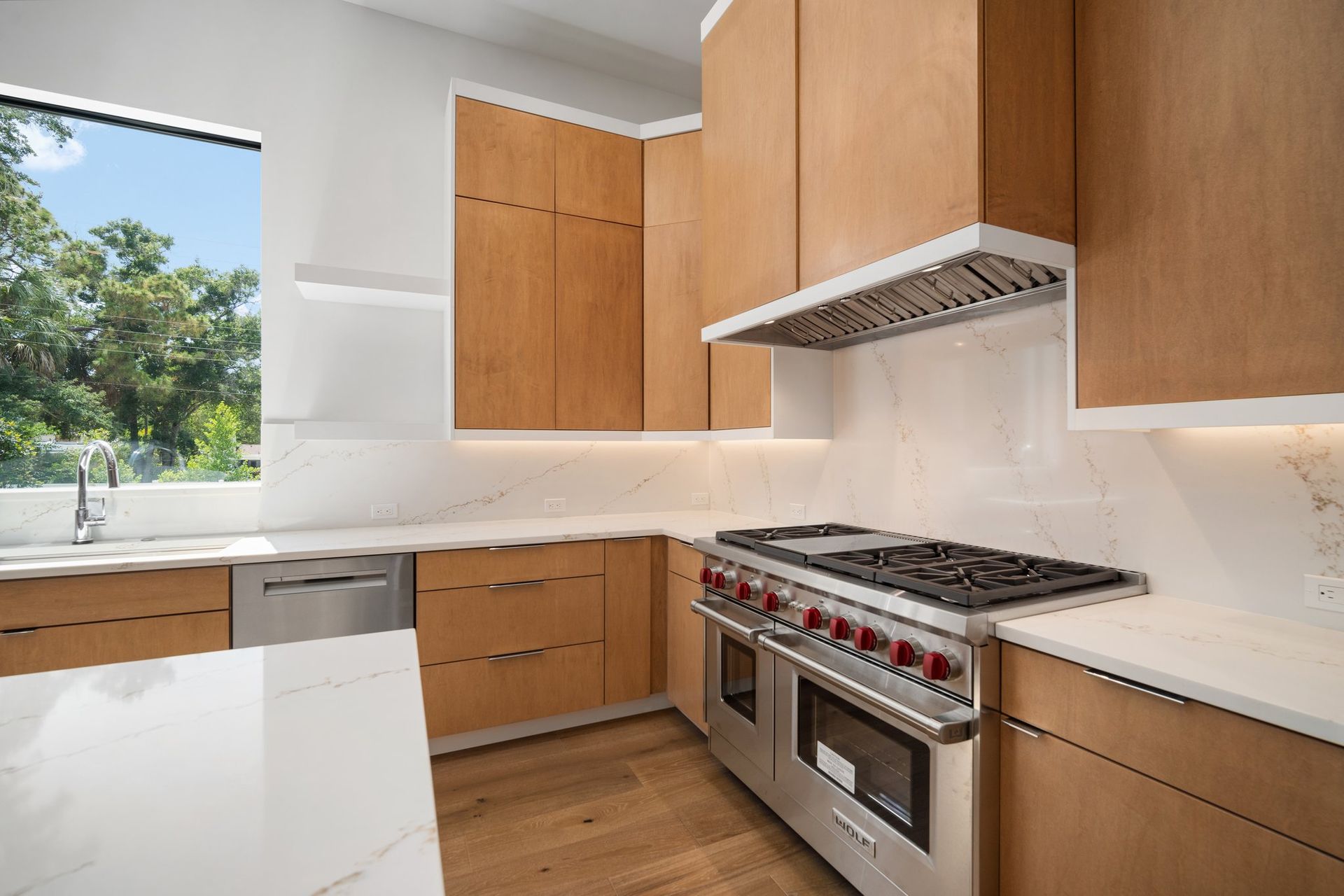 Modern kitchen with wood cabinets, white countertops, stainless steel stove, and a window view