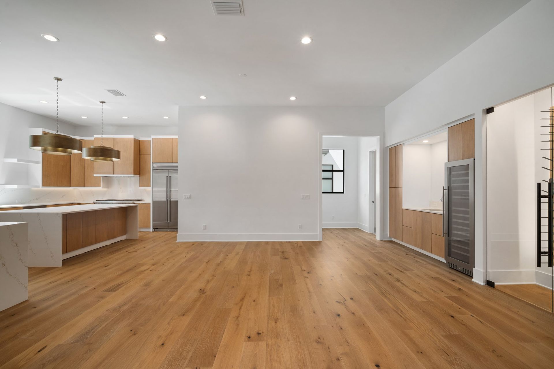 Bright modern empty kitchen and living area with wood floors, white walls, and built-in cabinets
