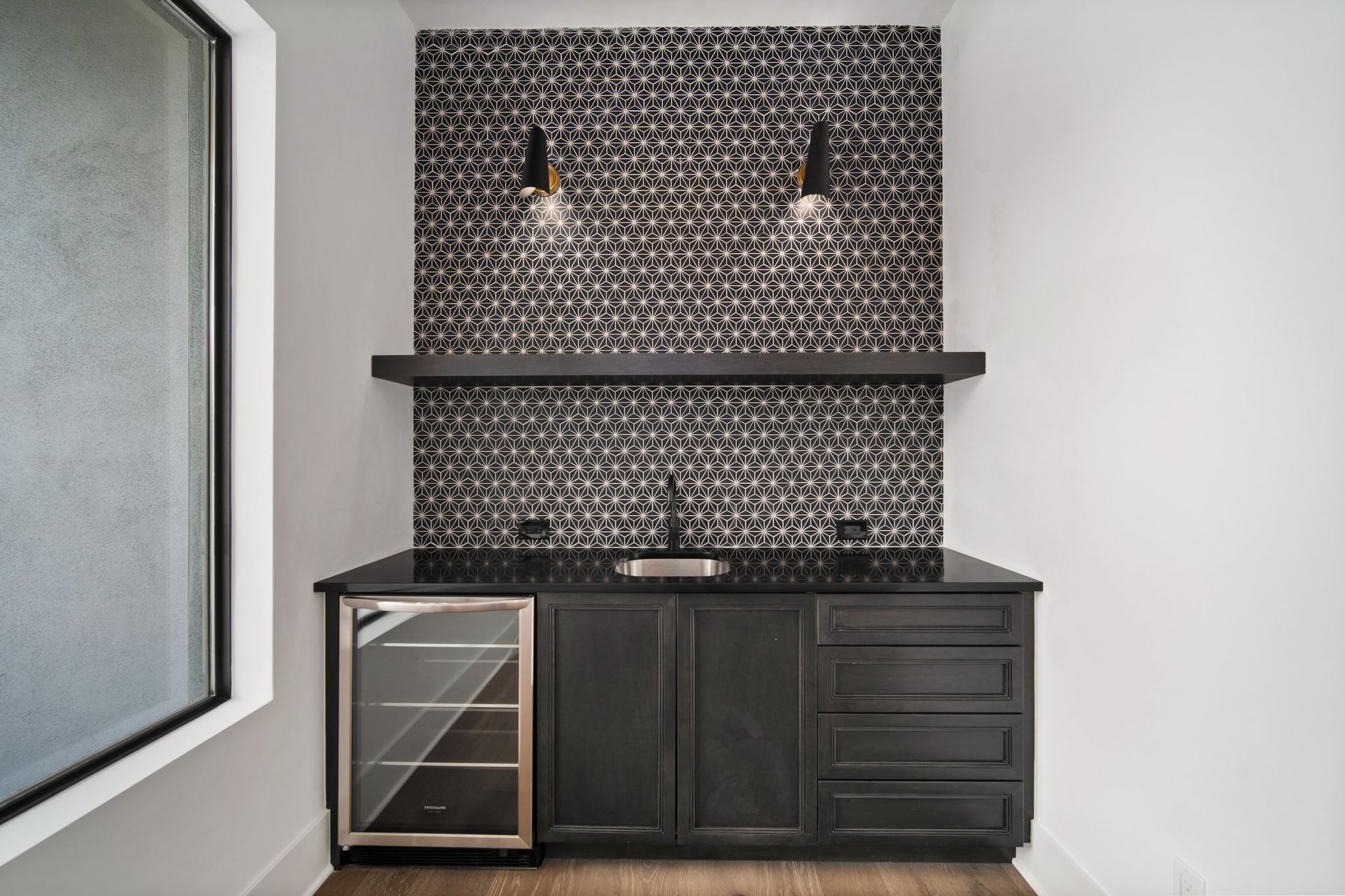 Modern dark bar cabinet with patterned backsplash, two pendant lights, and built-in wine cooler in a minimalist room