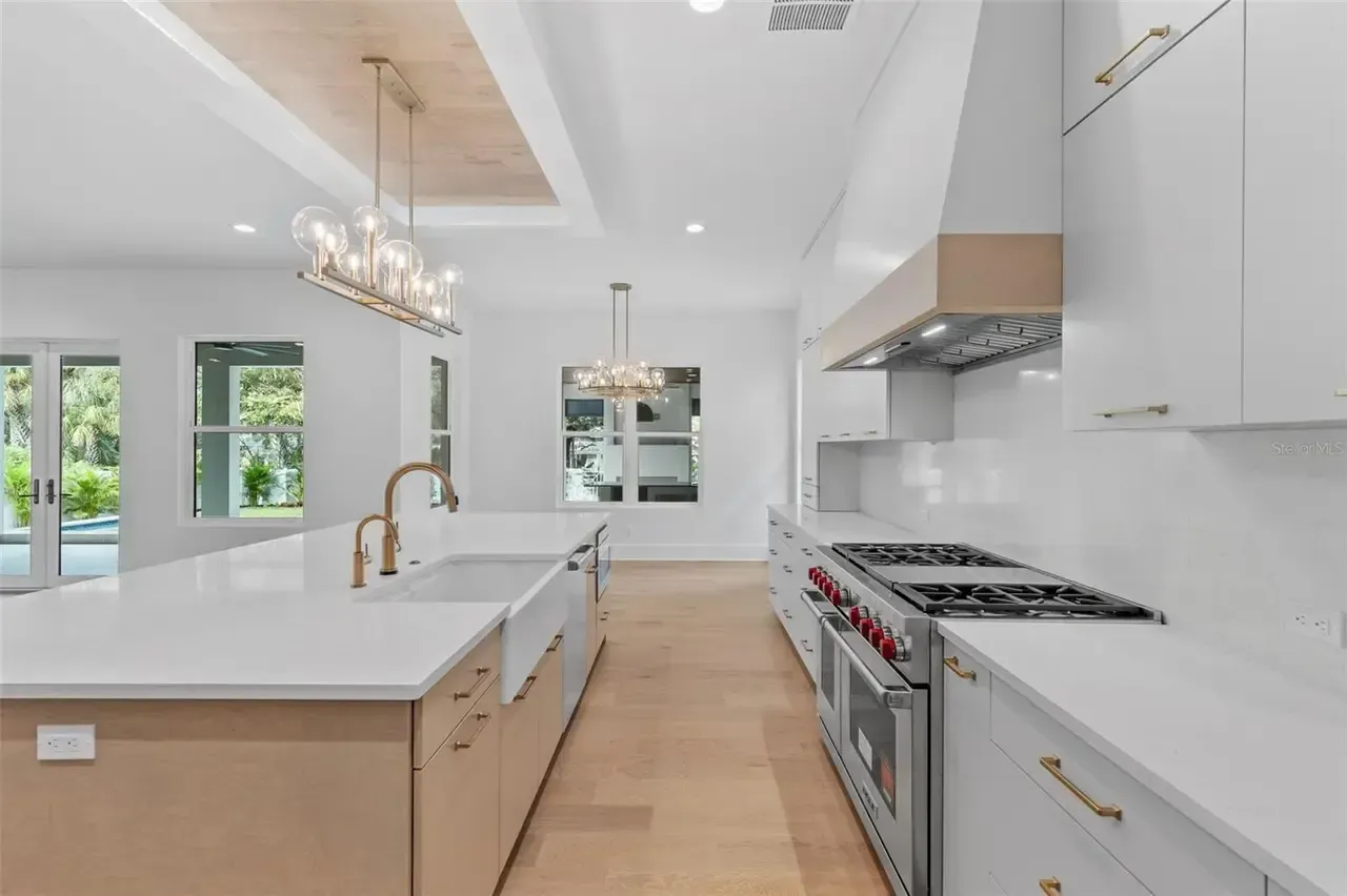 Bright modern kitchen with white cabinets, large island, gold fixtures, and stainless steel appliances