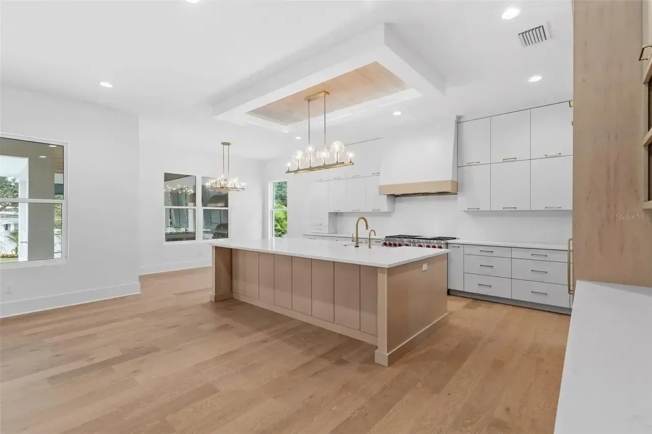 Bright modern kitchen with white cabinets, wood floors, and a large island under a tray ceiling.