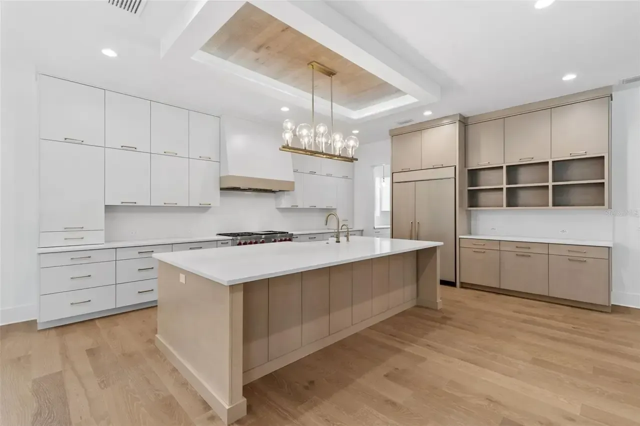 Bright modern white kitchen with island, built-in cabinets, wood floors, and chandelier