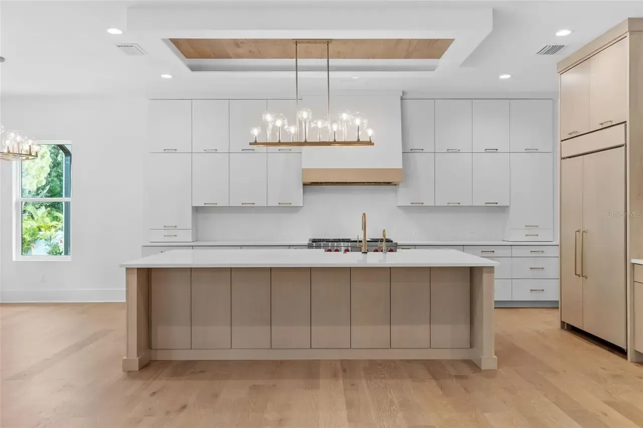 Bright modern kitchen with white cabinets, large island, pendant light, and built-in refrigerator.