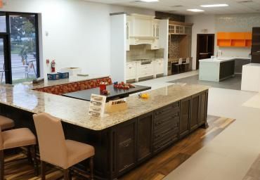 Modern kitchen showroom with a large island, white cabinets, and orange-accented counters