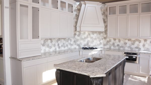 Bright white modern kitchen with a marble island, patterned backsplash, and stainless appliances.