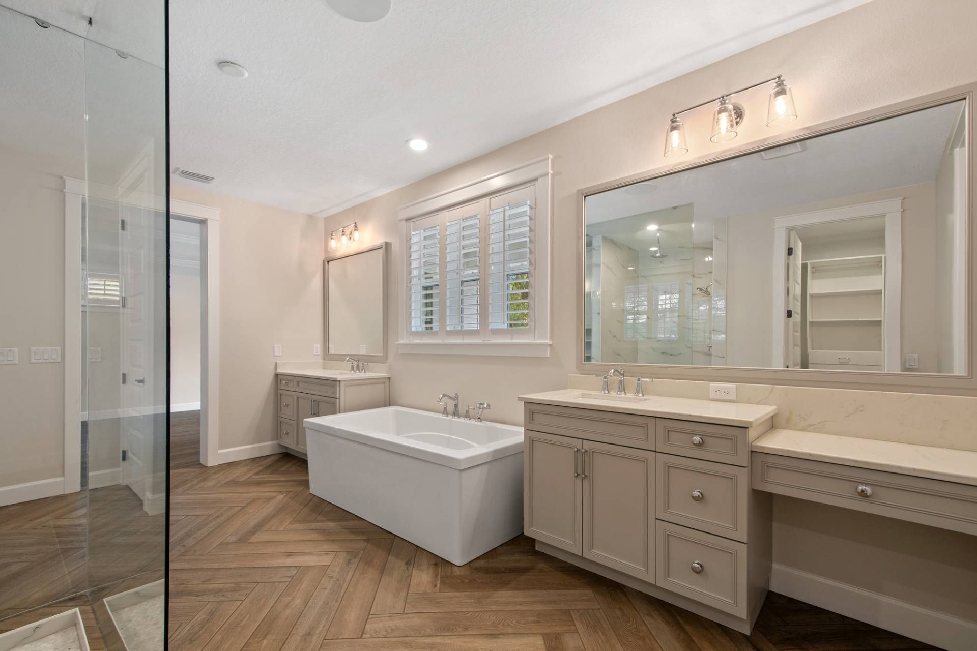Modern bathroom with freestanding tub, glass shower, double vanity, and light wood herringbone floor