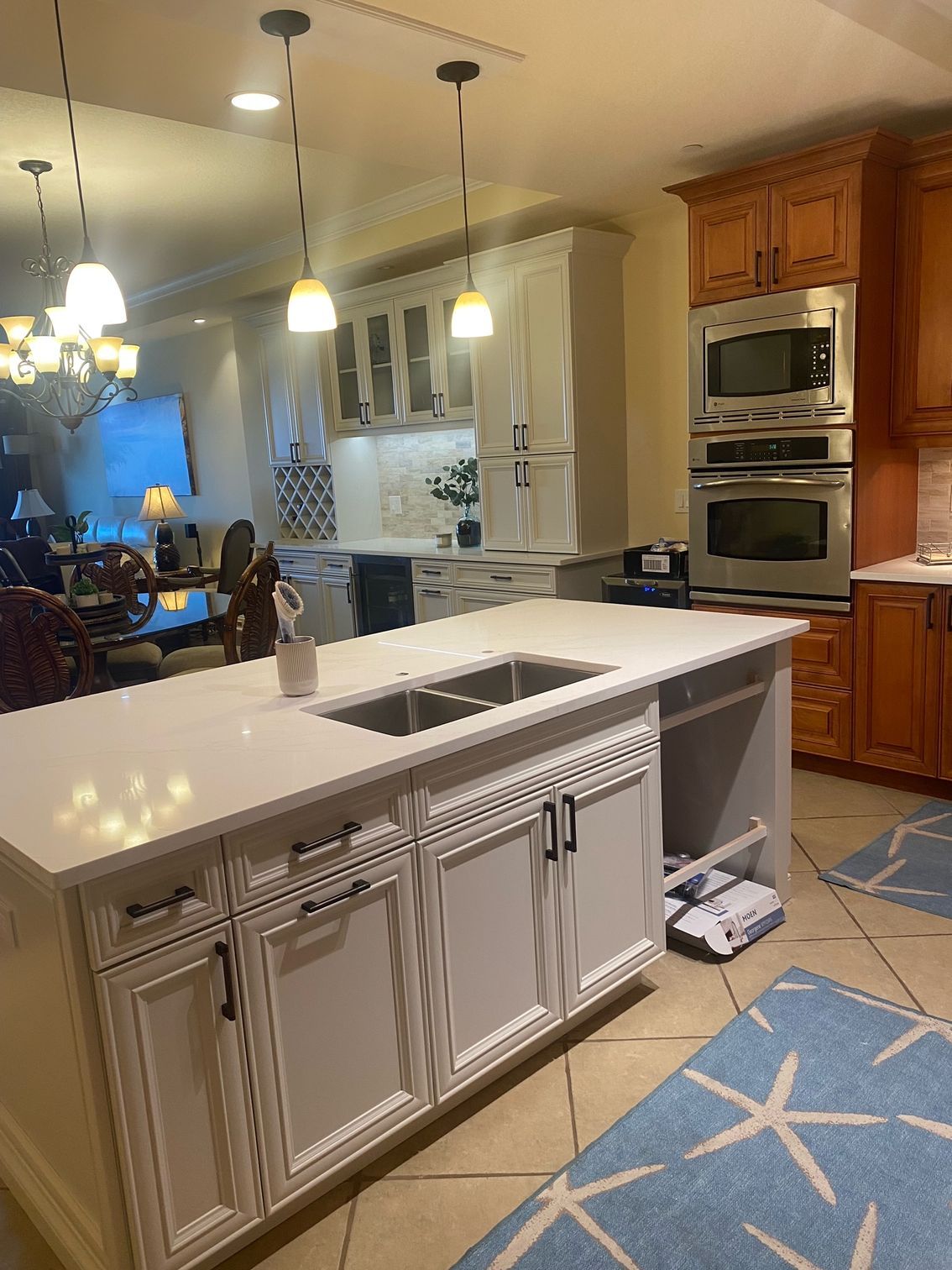 Bright kitchen with white island, pendant lights, wood cabinets, and blue patterned rug