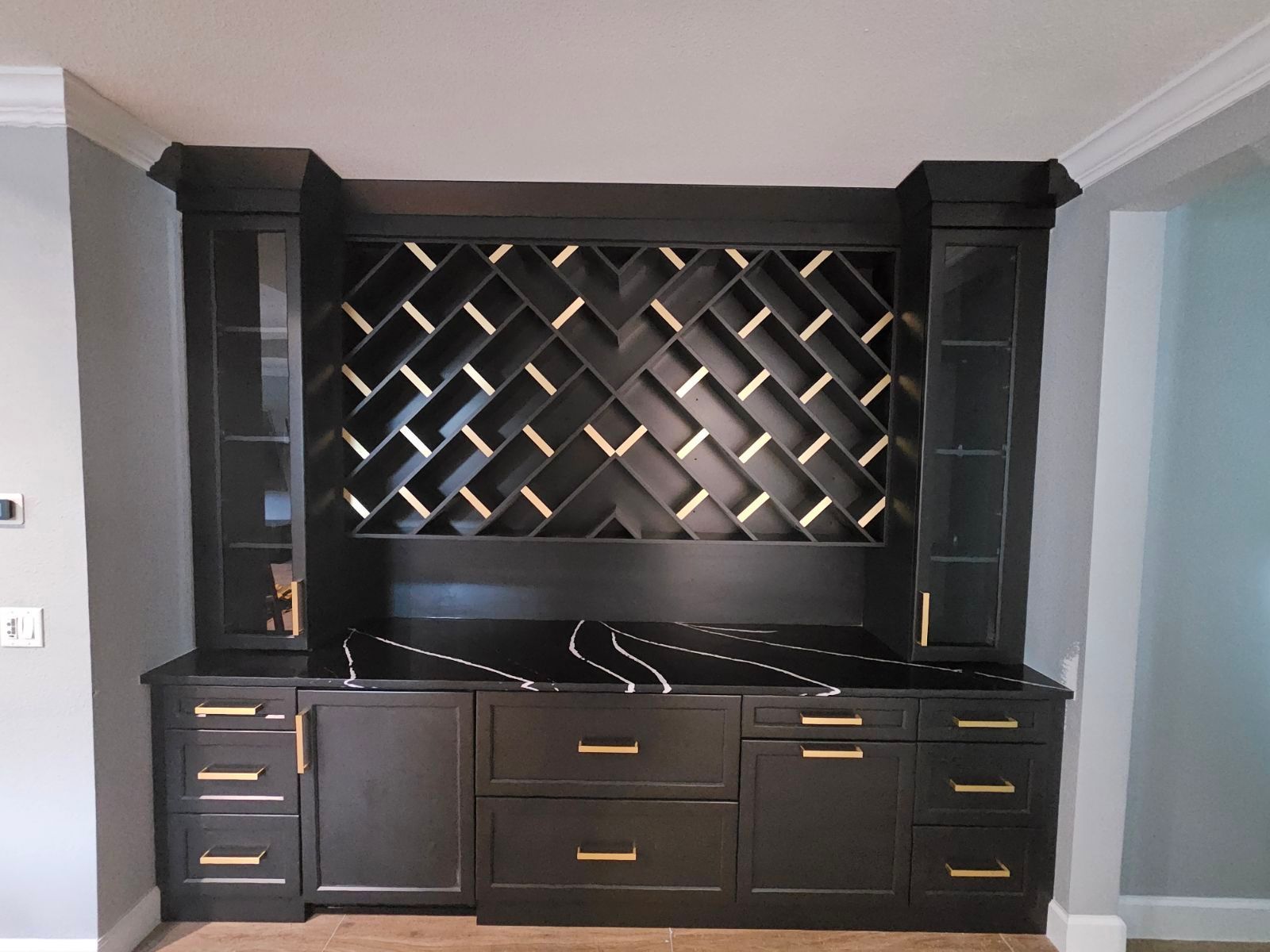 Black built-in entertainment center with shelves, cabinets, and a diamond-pattern backdrop in a living room.