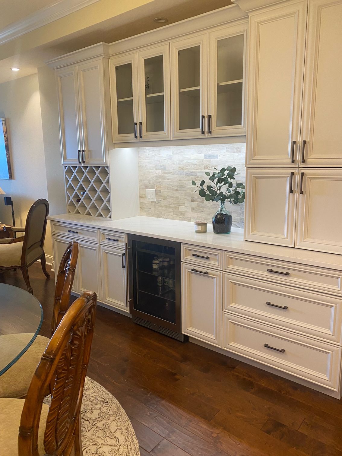 Elegant white kitchen with glass-front cabinets, wine rack, black dishwasher, and wood floor
