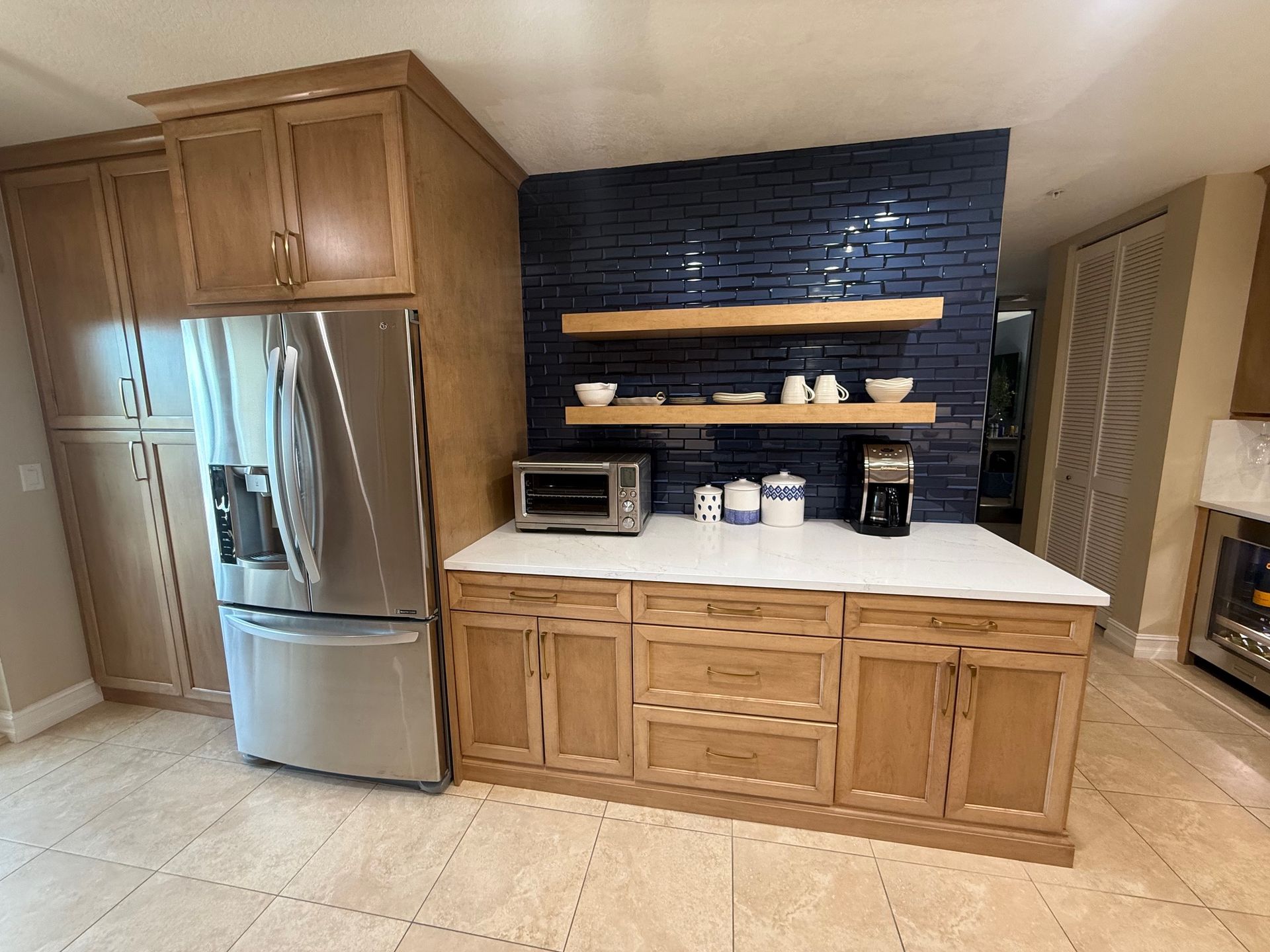 Kitchen with stainless steel fridge, wood cabinets, white countertop, and dark blue tile backsplash