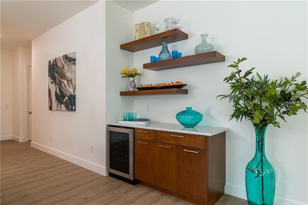 Modern hallway with wall art, floating shelves, a small cabinet, and a turquoise vase with greenery