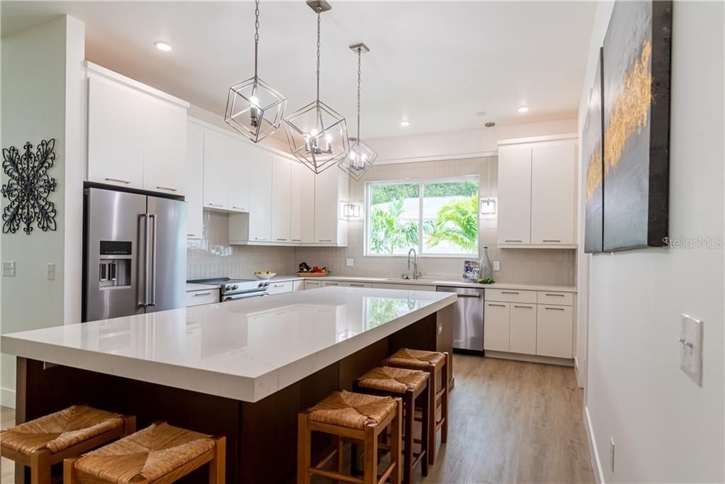 Bright modern kitchen with white cabinets, large island, bar stools, and stainless steel appliances