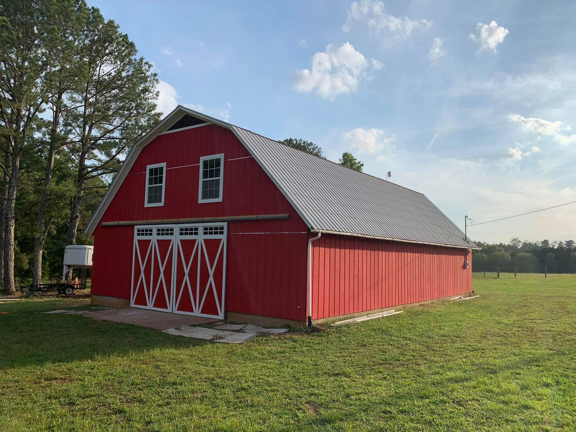 Red barn with white trim and large doors in a grassy field under a partly cloudy sky
