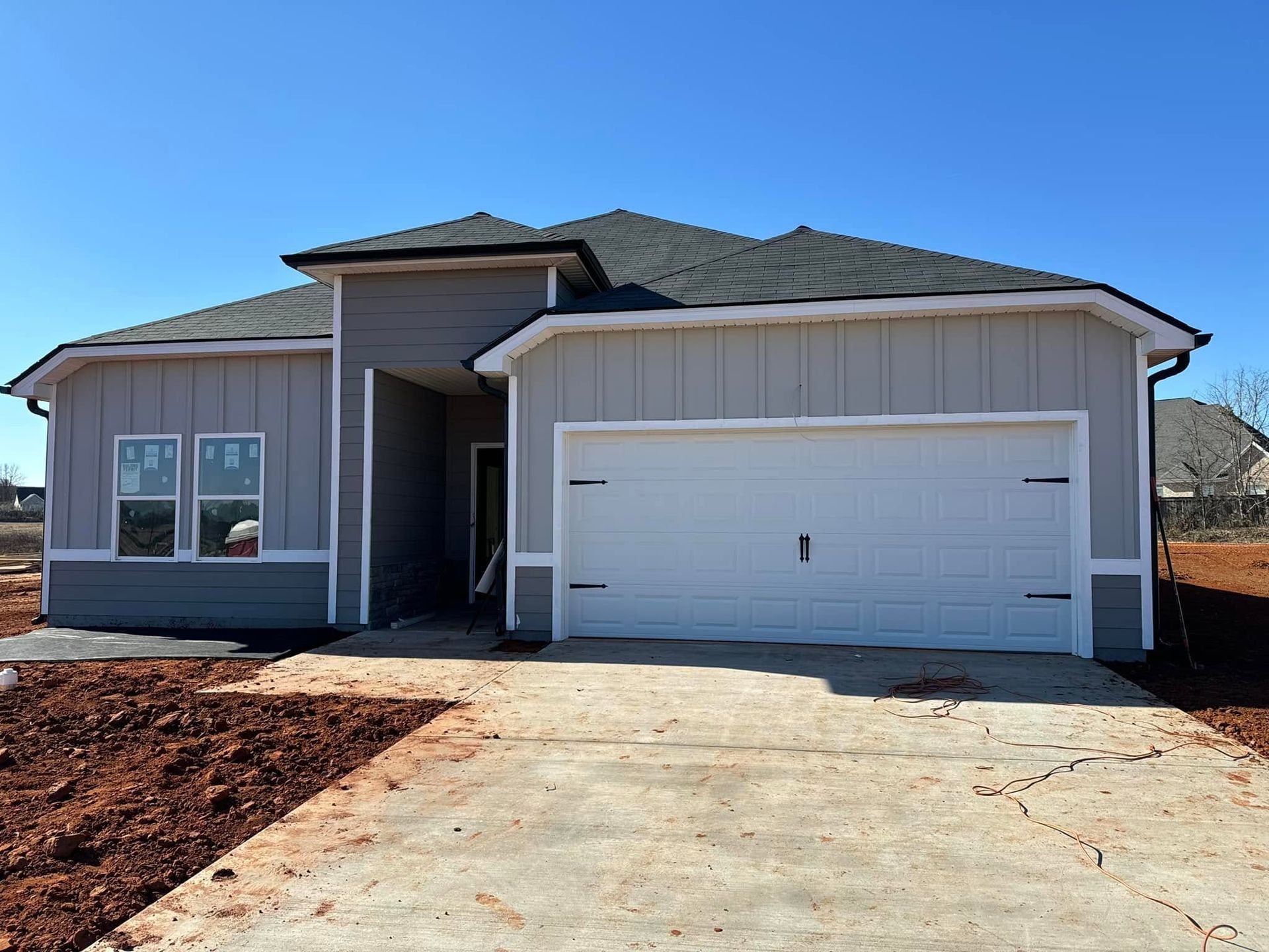 Single-story beige house with a white garage, driveway, and front entry under a blue sky