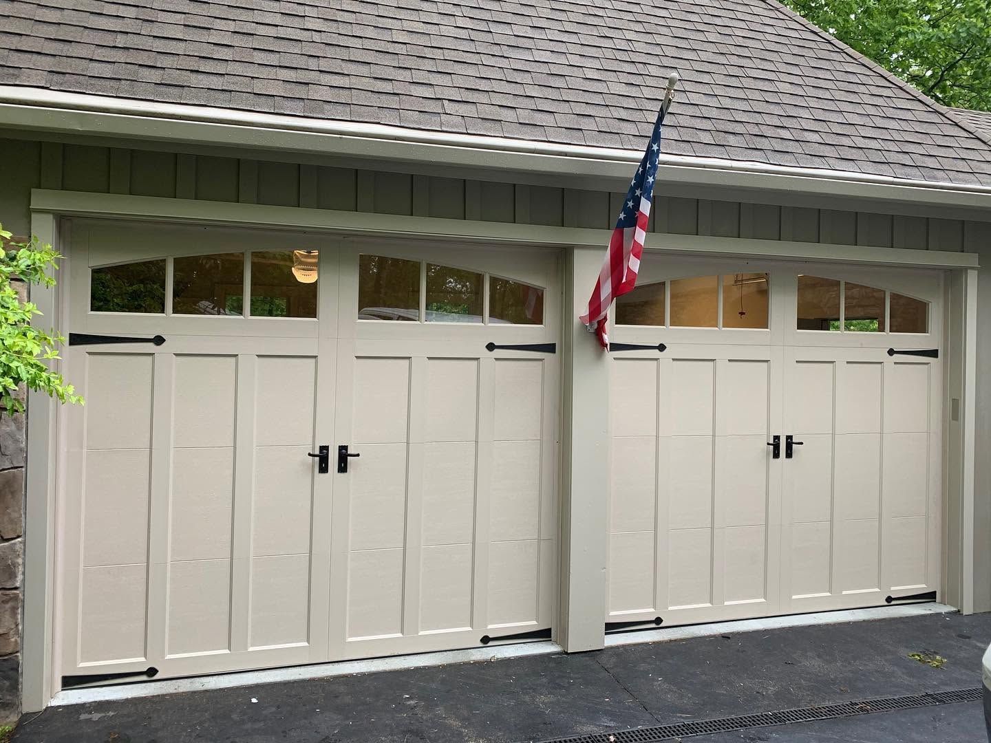 Two beige garage doors with arched windows and an American flag above them