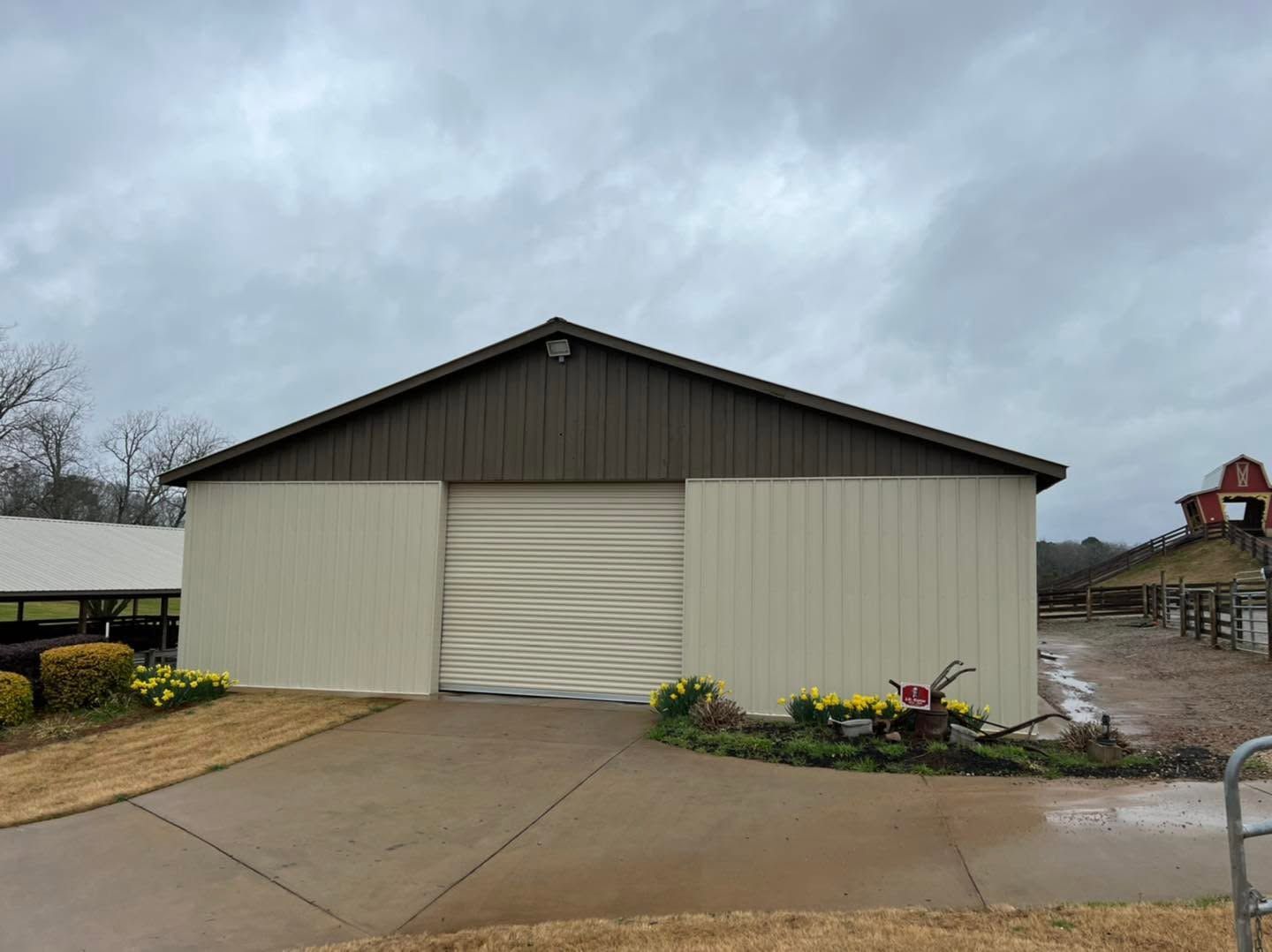 Gray metal warehouse with a large roll-up door on a wet concrete lot under cloudy skies