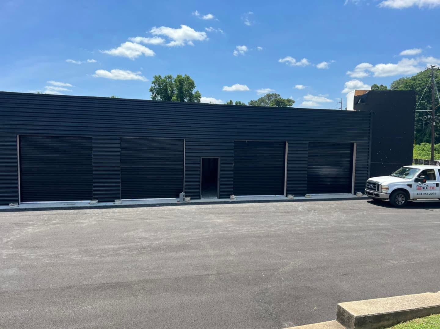 Black commercial building with parking lot, blue sky, and a white SUV parked at right