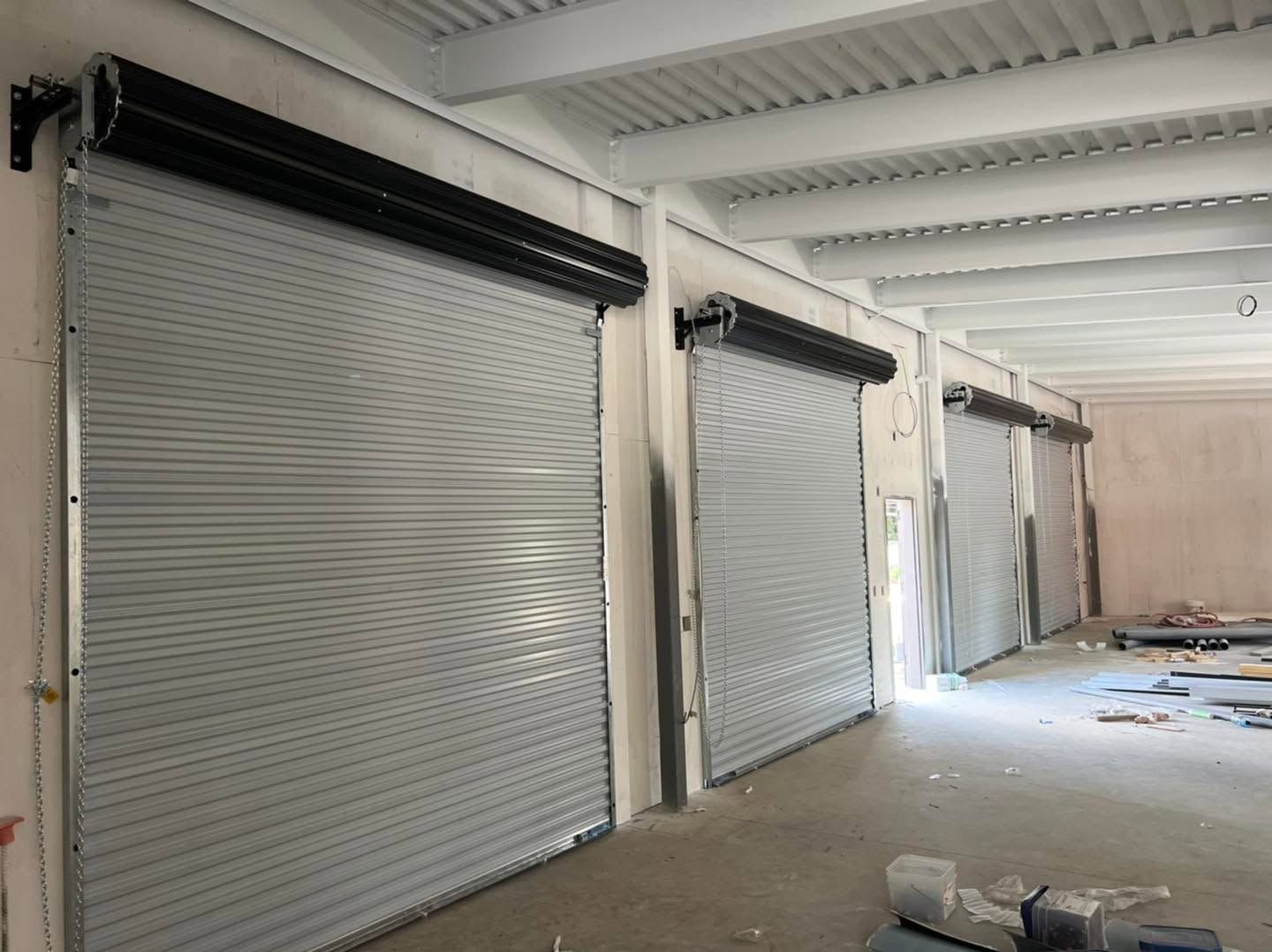 Row of closed gray metal roll-up doors in an unfinished industrial hallway