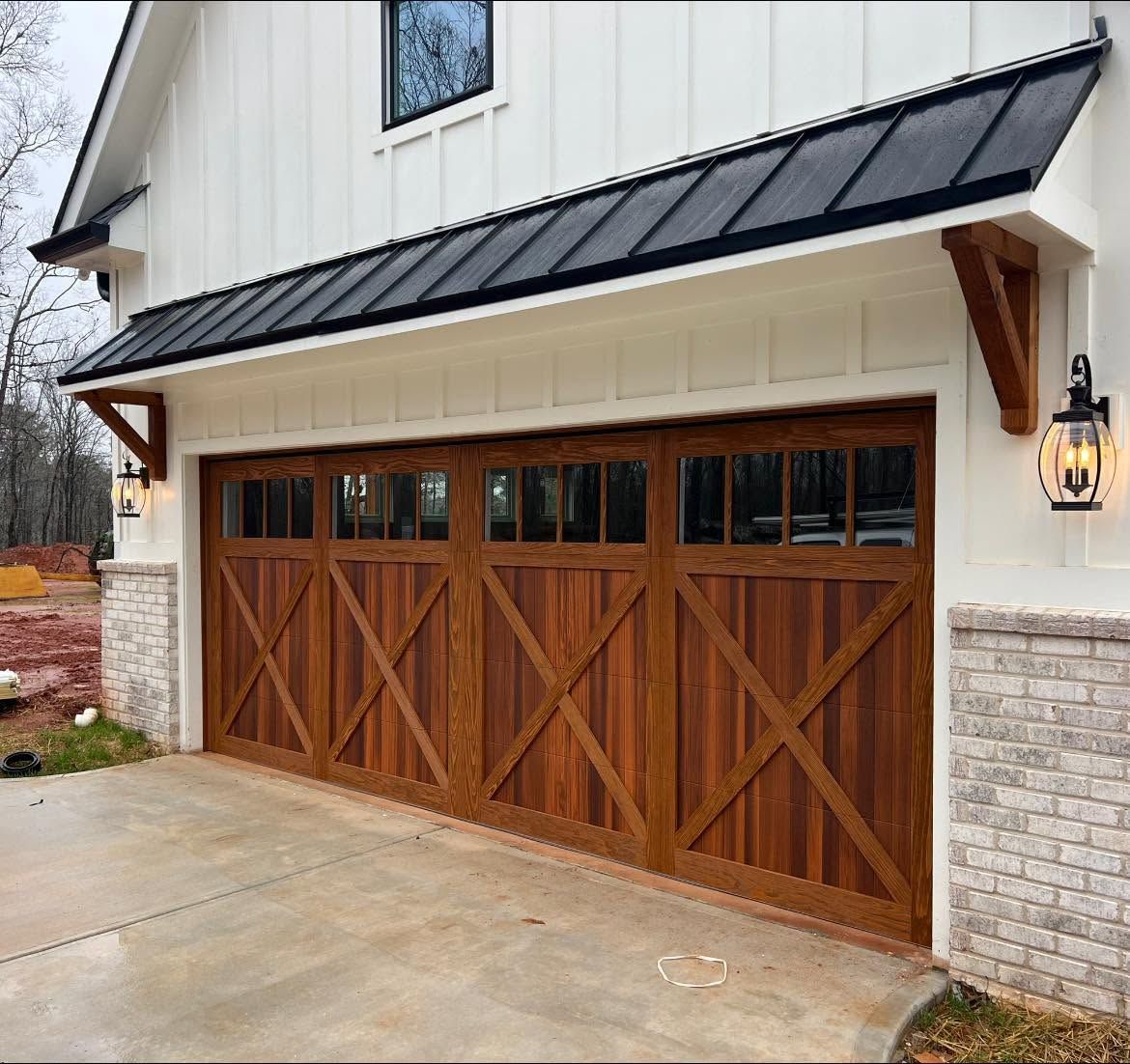 Wooden double garage doors beneath a black metal awning on a cream-colored house exterior