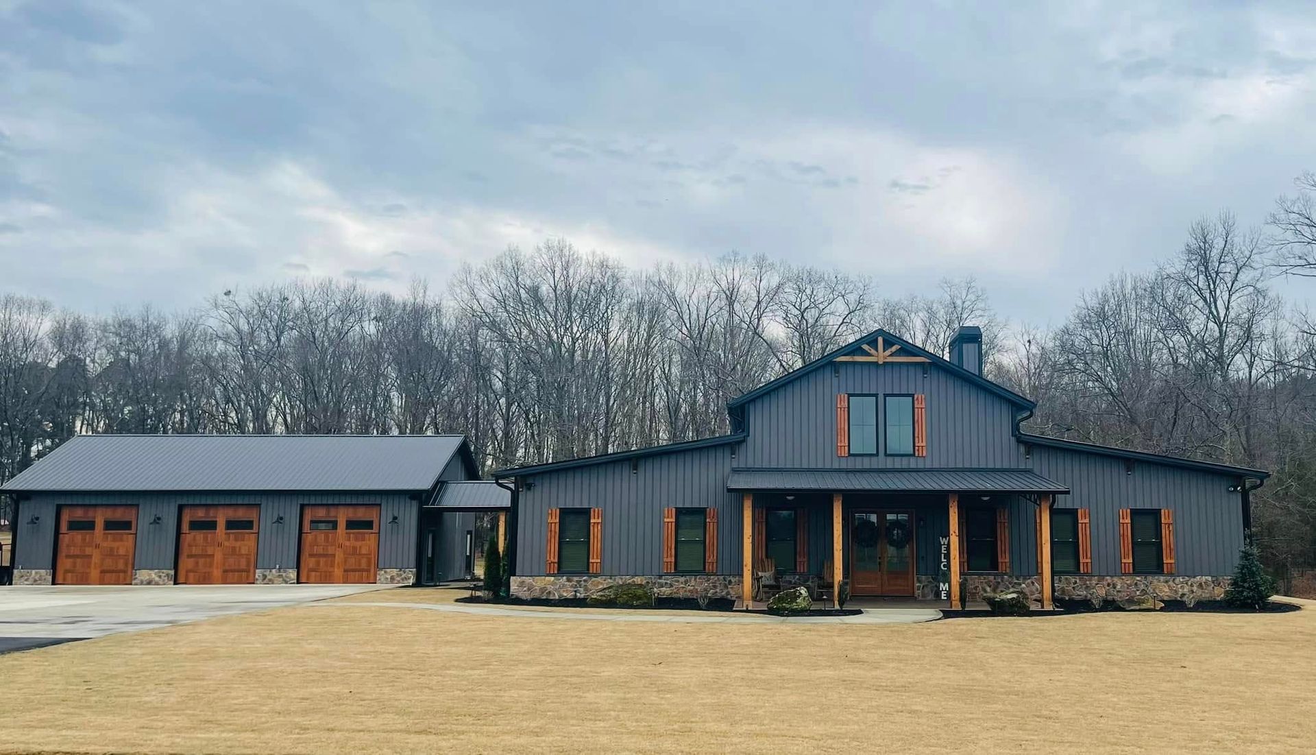 Large gray house with a covered porch and attached garage on a grassy lot under an overcast sky