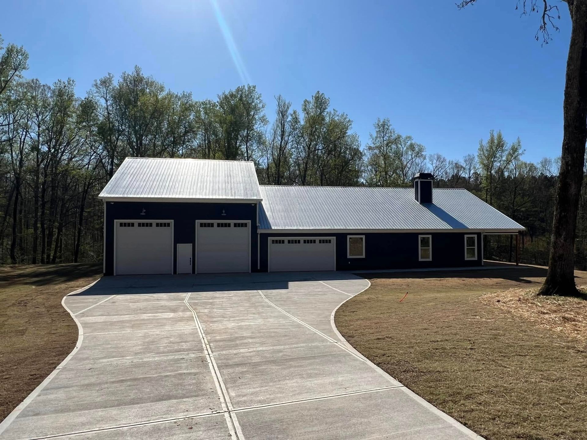 Newly built white barn-style garage with concrete driveway and trees under a clear blue sky