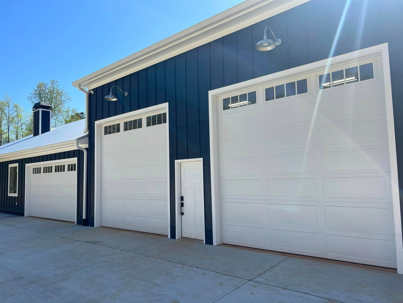 Three white garage doors on a dark blue industrial building under a sunny sky.