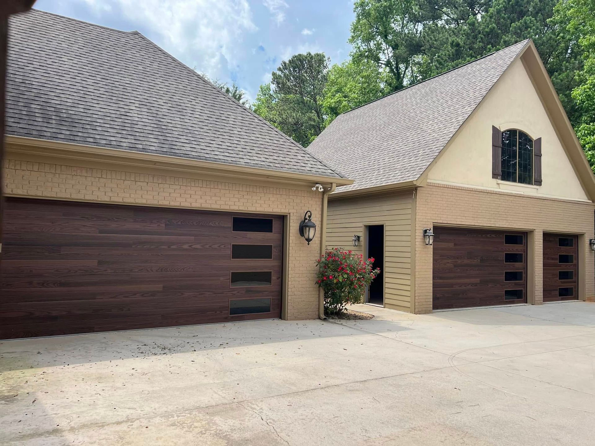 Two beige houses with dark brown garage doors and a driveway under a tiled roof
