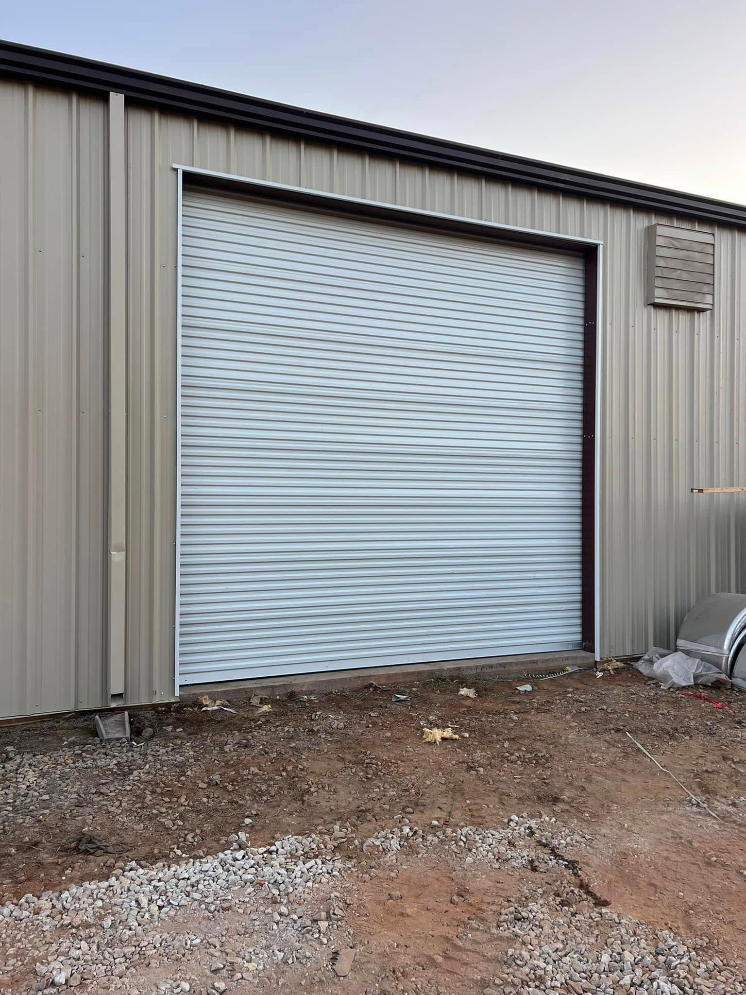 Metal building exterior with a closed white roll-up garage door and gravel in front