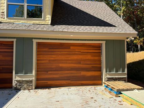 Two-car garage with wooden doors and green siding beside a house, viewed from the driveway.