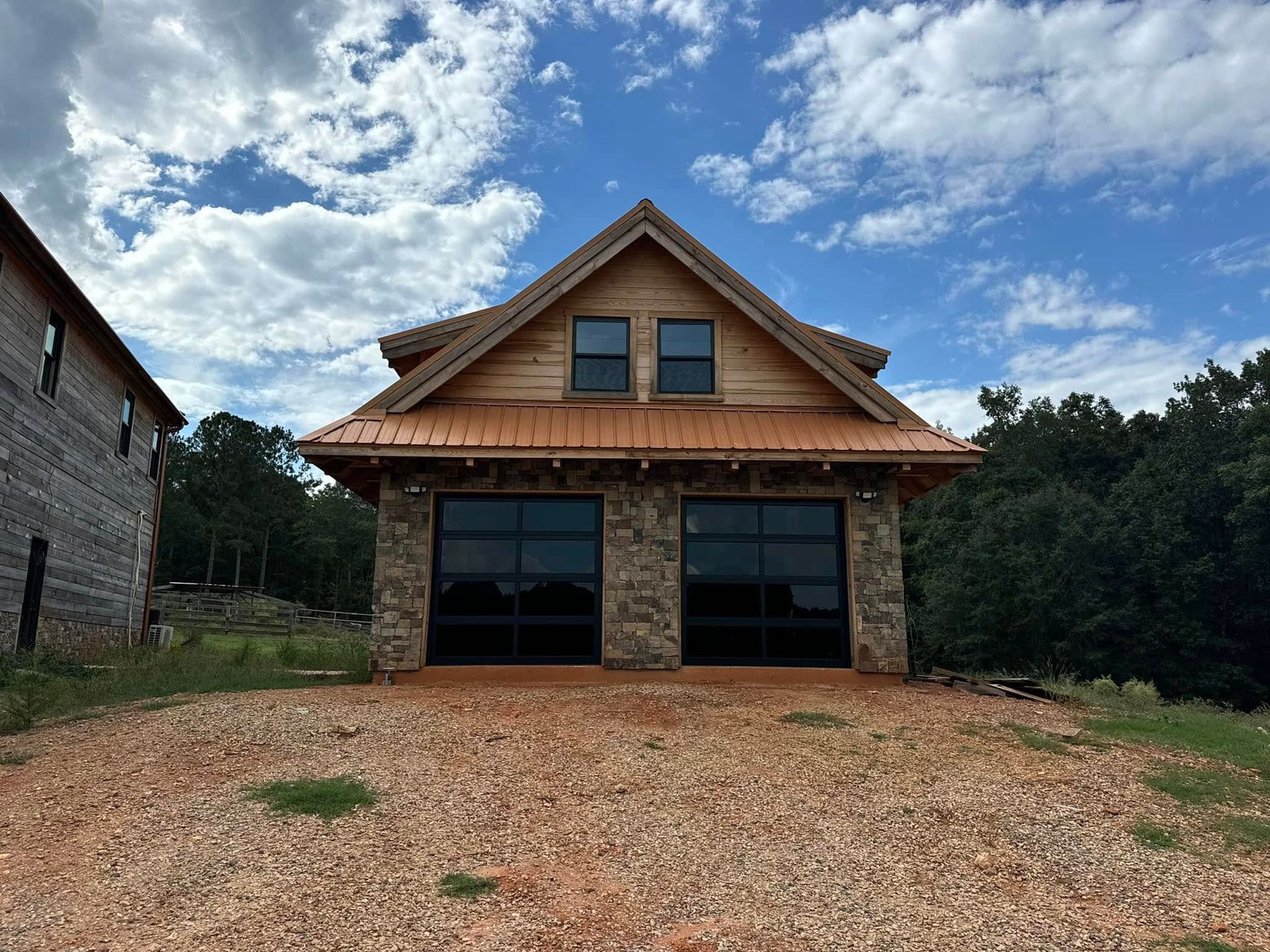 Stone-and-wood house with a steep roof, large windows, and a gravel driveway under a cloudy sky.