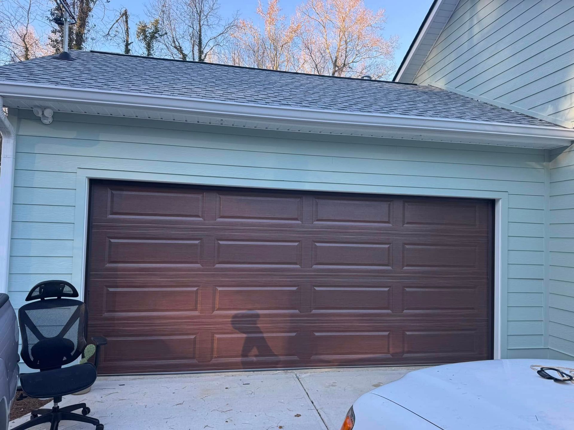 Single-car garage with a brown door, light blue siding, and a stroller beside it.