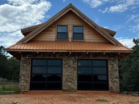 Stone-front cabin with two large dark garage doors and two windows under a gabled roof