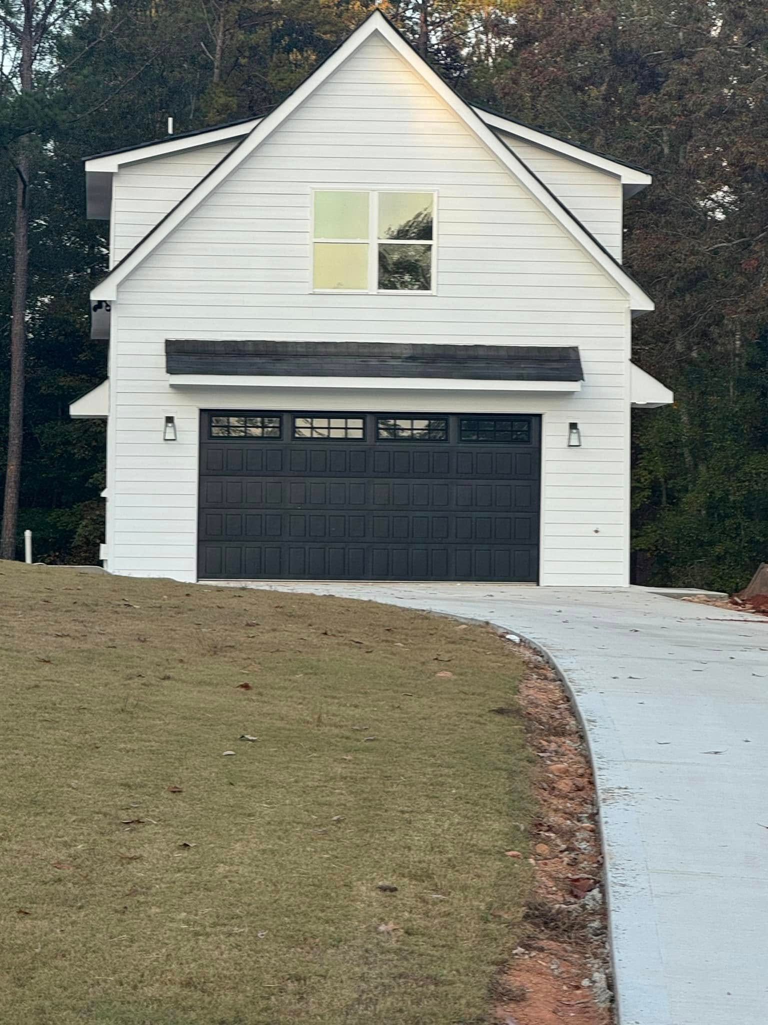 White house with black garage door and curved driveway in front of a grassy yard
