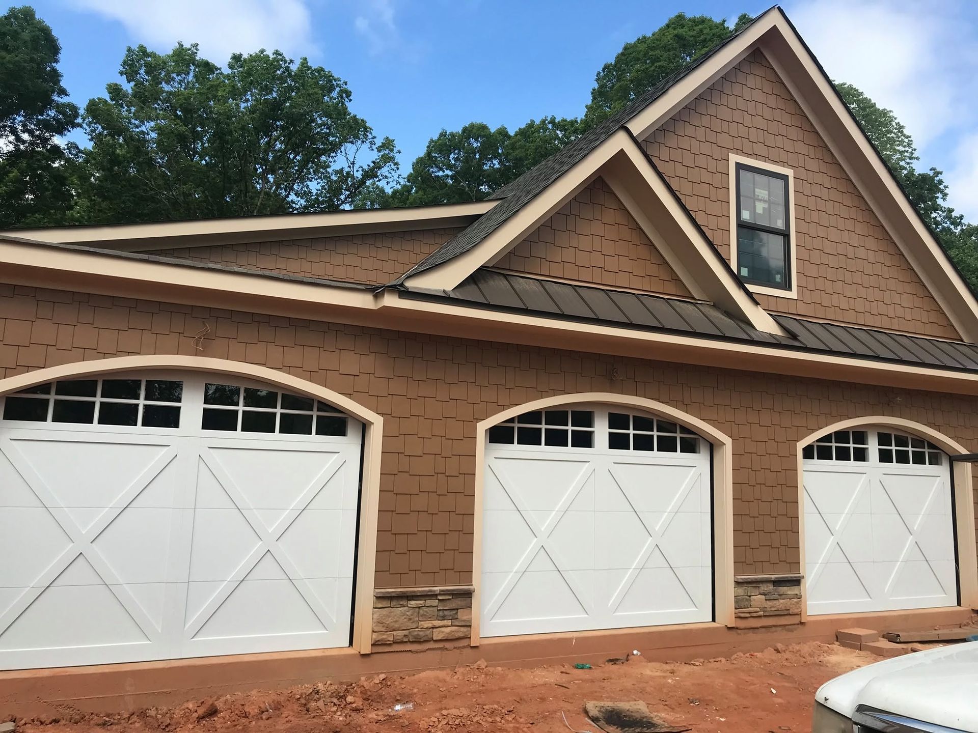 Three white garage doors on a tan brick house with a steep roof and arched windows