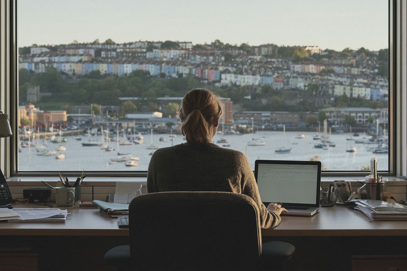 Commercial professional working at a laptop by a window overlooking a harbour