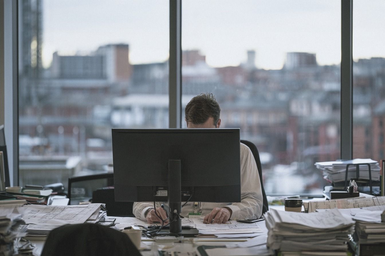 Quantity surveyor marking up drawings behind a computer monitor in a city office