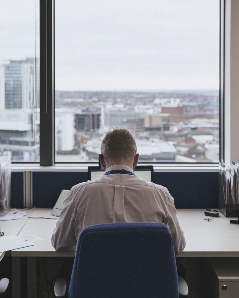 Quantity surveyor working at a desk by an office window on an overcast day