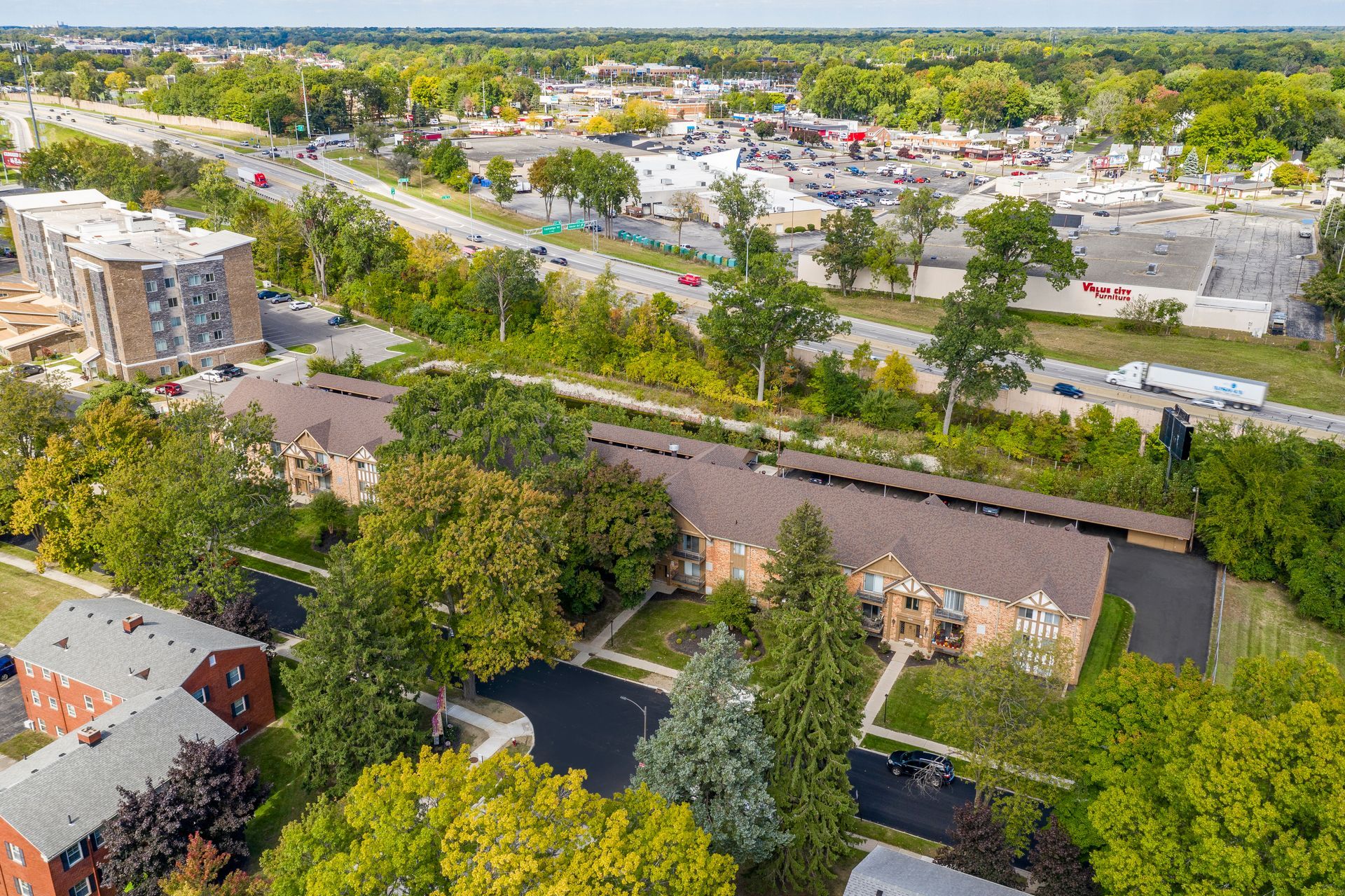 Aerial view of apartment buildings with surrounding greenery and commercial area in the background.