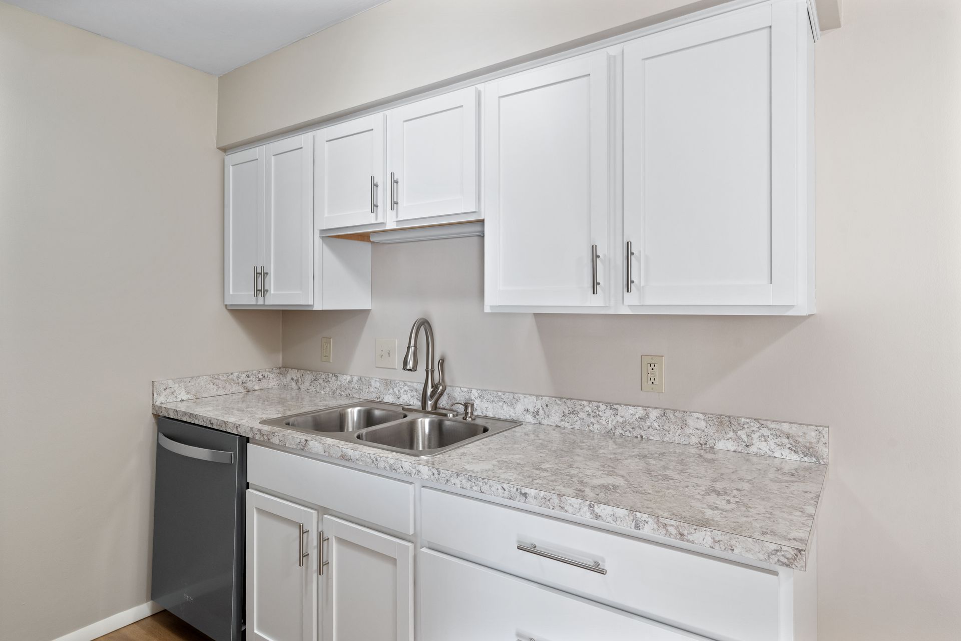 White kitchen cabinets, gray countertop, stainless steel sink and faucet.