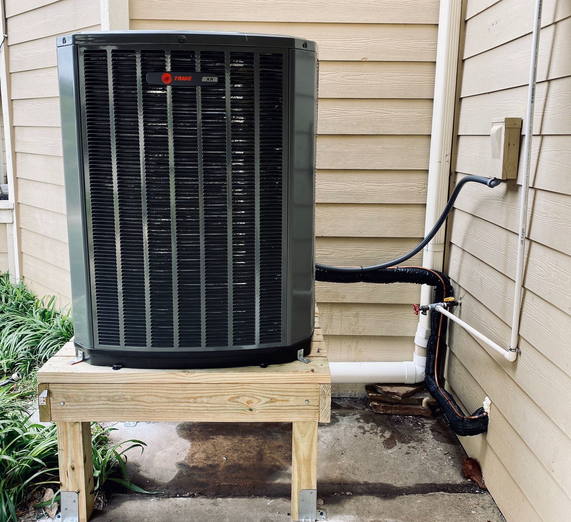An air conditioner is sitting on a wooden stand outside of a house.